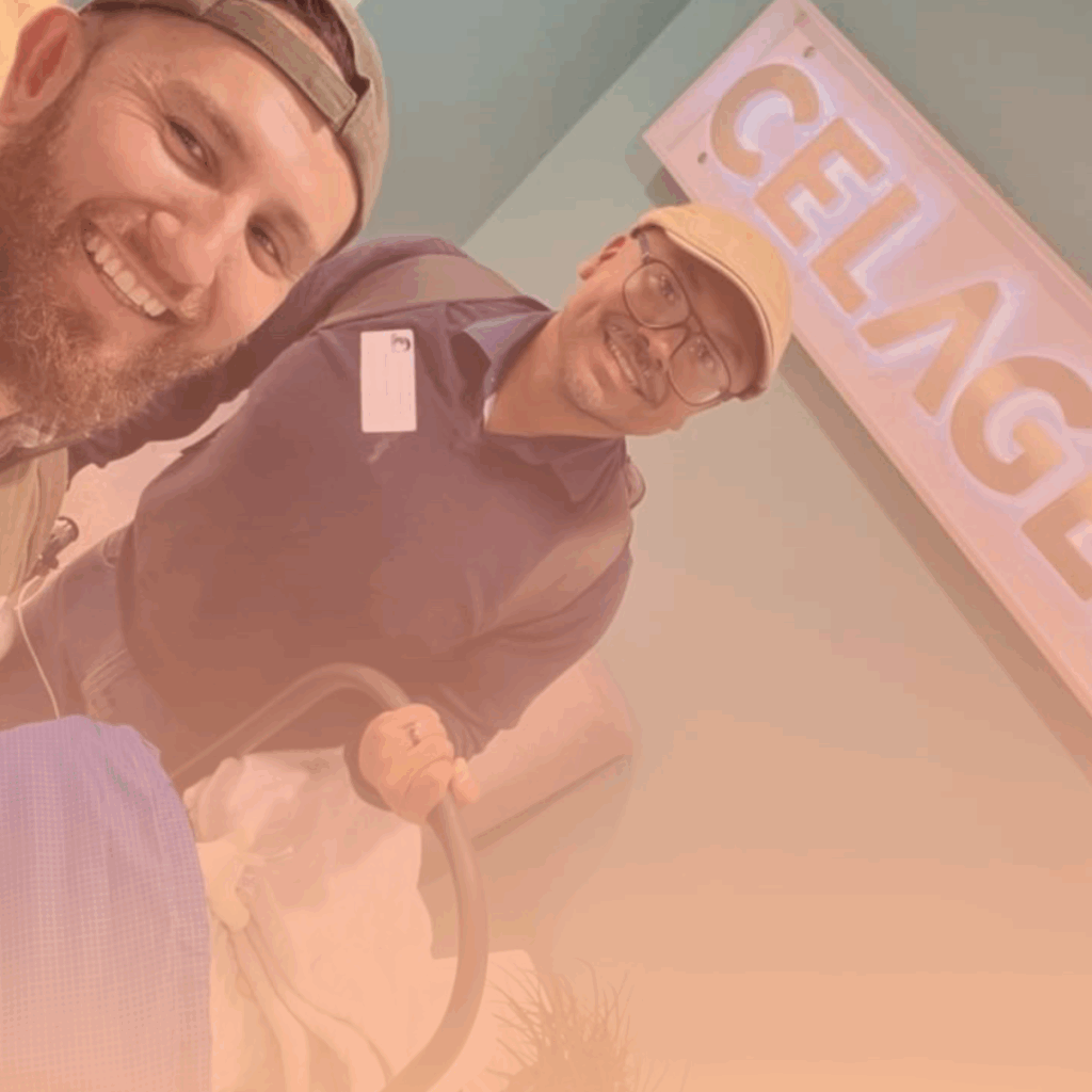 Two gay dads holding their newborn in a baby carrier, smiling in front of CELAGEM fertility clinic sign in Bogotá, Colombia.